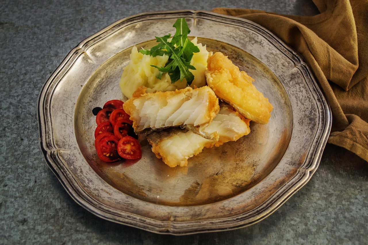 Bacalao rebozado con puré de papas y tomates cherry, servido en un plato gourmet