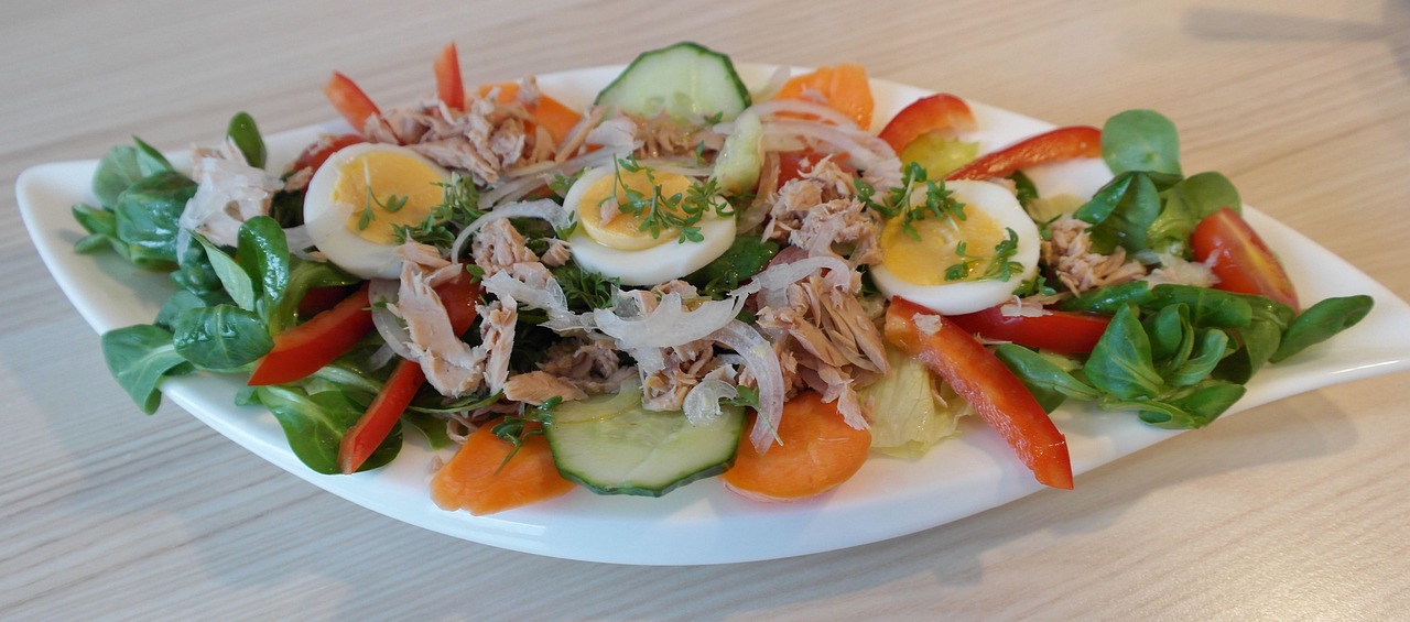 Ensalada fresca con atún desmenuzado, huevo duro, rodajas de pepino, zanahoria, pimiento rojo y hojas verdes servida en un plato blanco