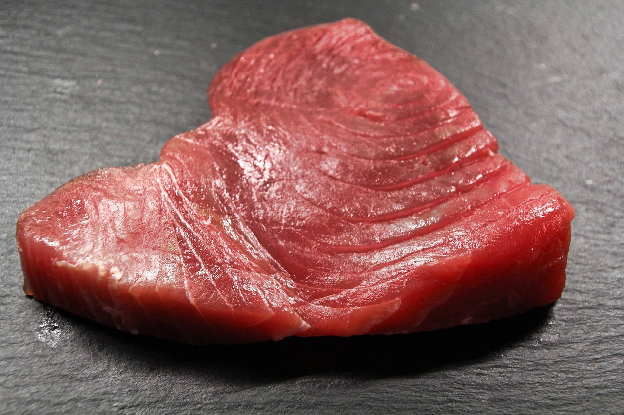 Filete fresco de atún rojo crudo sobre una superficie oscura, mostrando la textura y color intenso de la carne