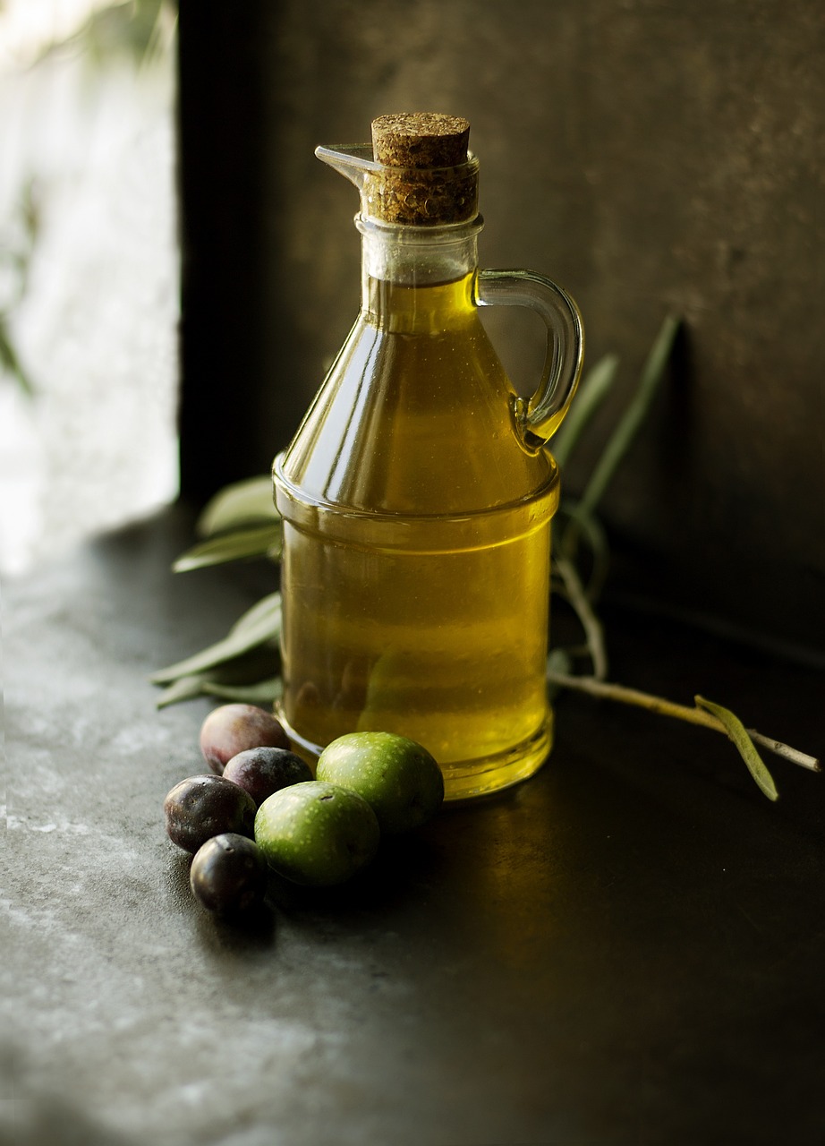 Botella de aceite de oliva con aceitunas verdes y negras sobre una superficie oscura.